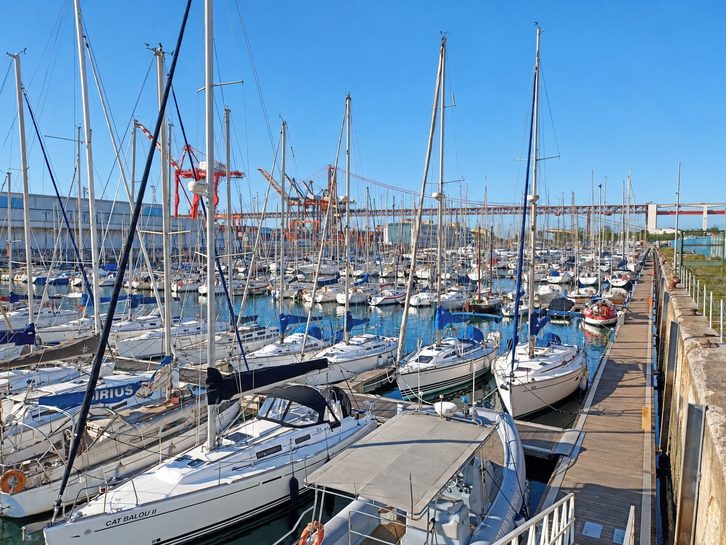 Ein Yachthafen mit vielen vertäuten Booten, einer Holzpromenade und einer Brücke im Hintergrund.