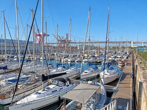 Un puerto deportivo con numerosas embarcaciones amarradas, un muelle de madera y un puente al fondo.