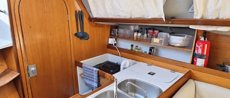 Una kitchenette compacta con lavamanos, estufa y estantes de almacenamiento.