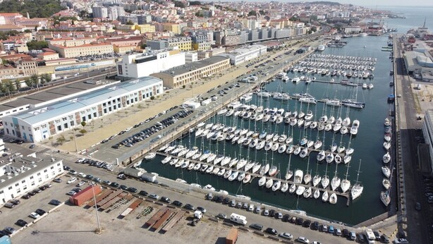 Un port de plaisance où sont amarrés de nombreux bateaux, un espace de stationnement et des bâtiments en arrière-plan.