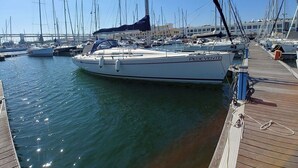 Un port de plaisance où sont amarrés de nombreux voiliers, une jetée en bois et un ciel bleu azur.