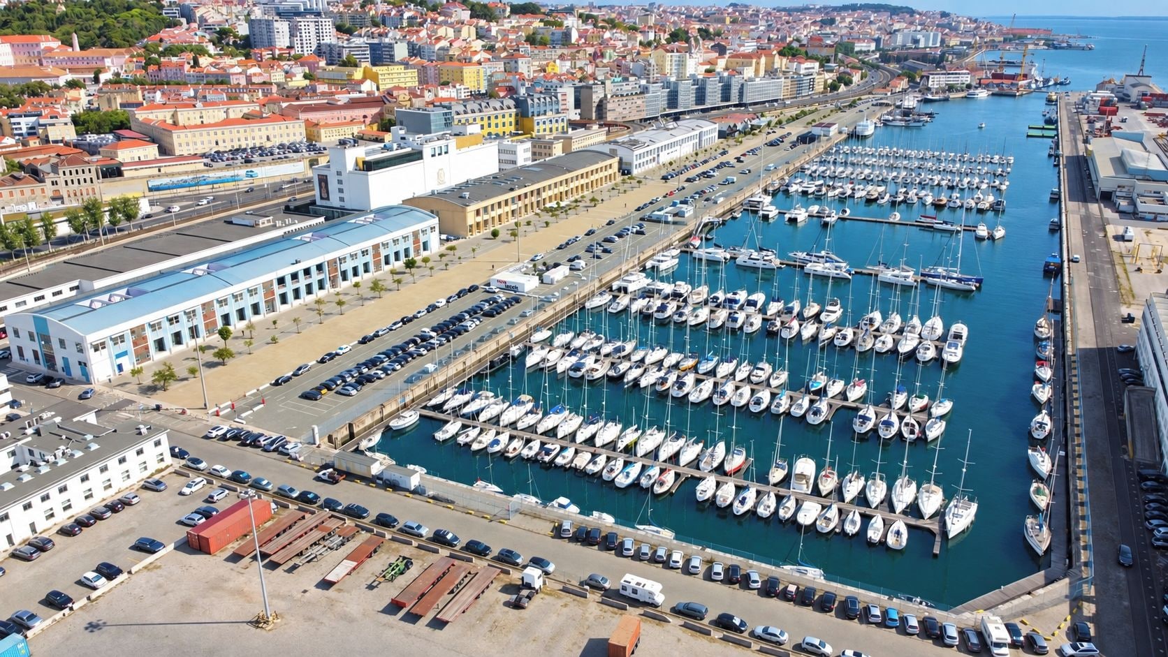 Un port de plaisance où sont amarrés de nombreux bateaux, un parking rempli de voitures et, au loin, une vue sur la ville.