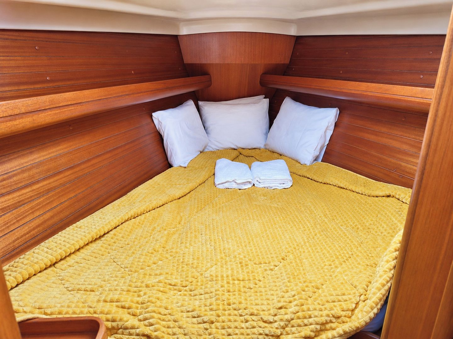 A compact bed with a yellow textured blanket and white pillows in a wooden cabin-style room.
