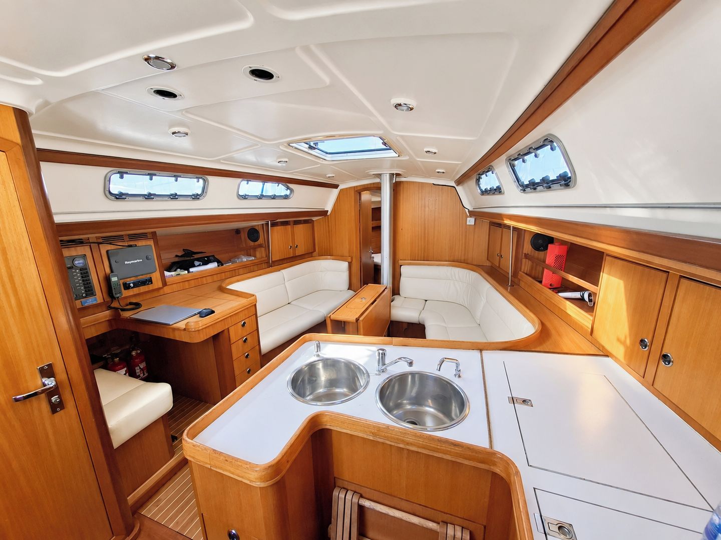 A boat interior with a dining area, two seating areas, a kitchen with a sink, and a control panel.