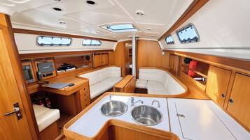 A boat interior with a dining area, two seating areas, a kitchen with a sink, and a control panel.