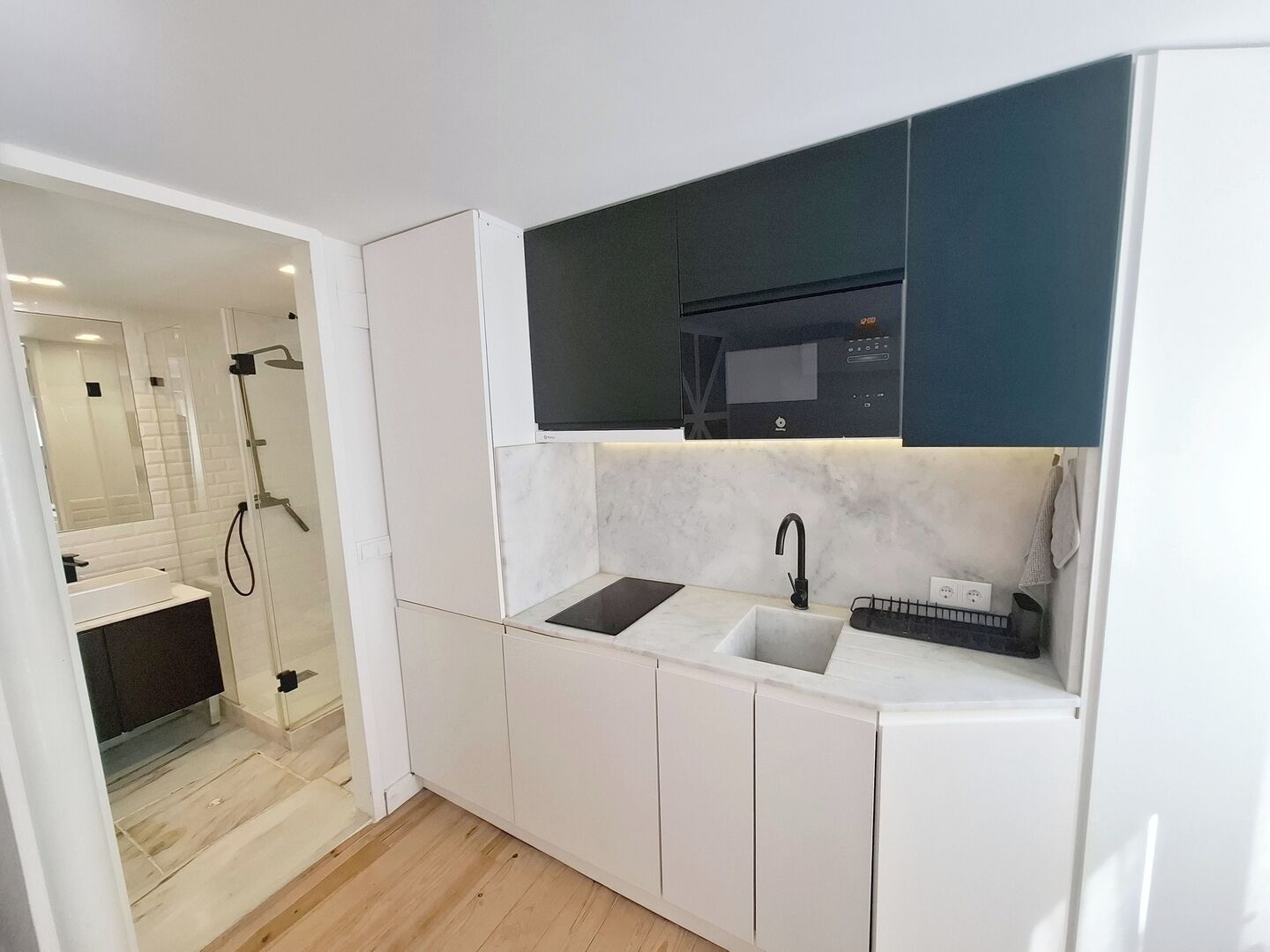 A modern kitchen with white cabinetry, a black microwave, and a built-in sink.