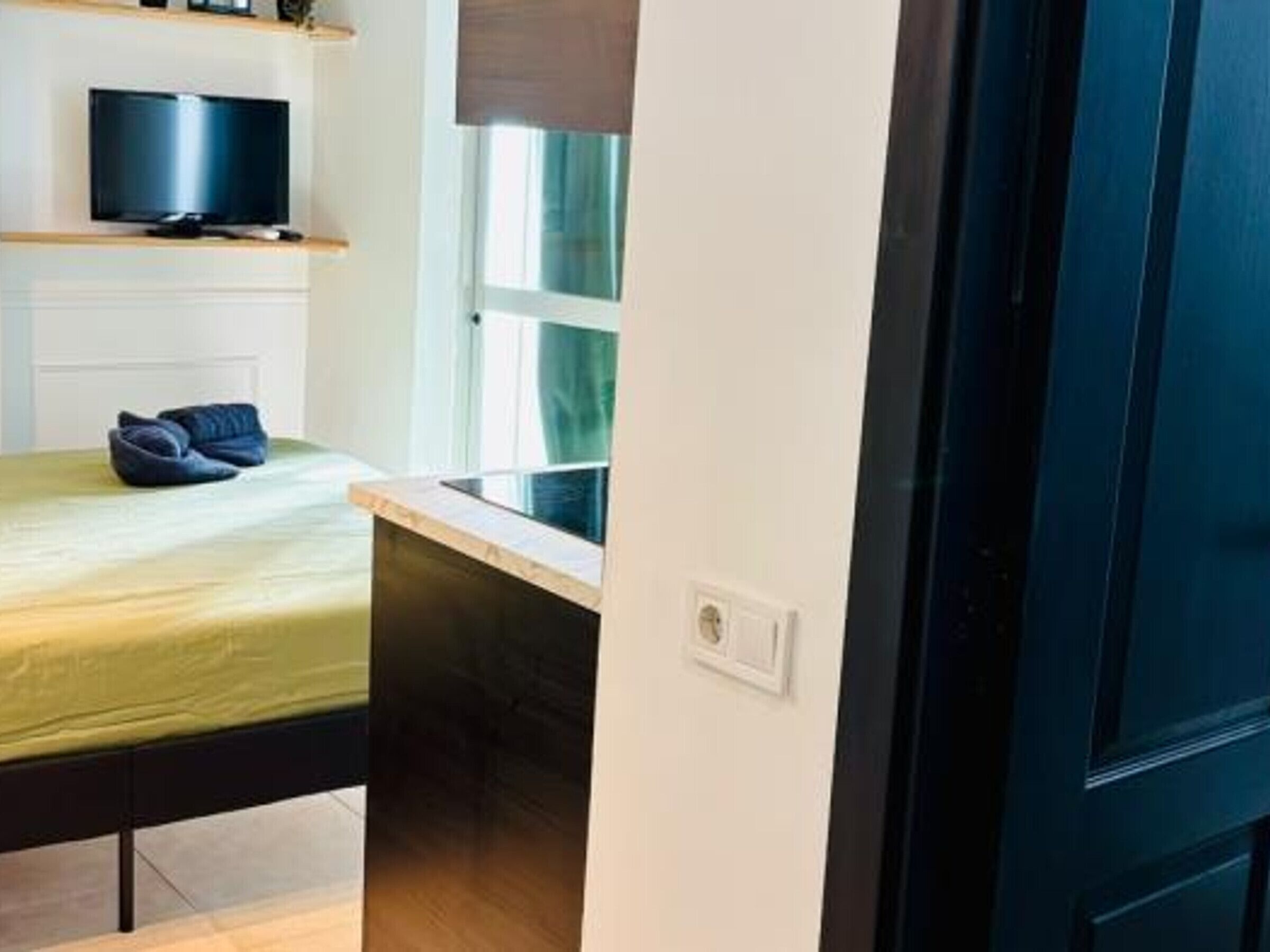 A small room with a bed, a television on a shelf, and a window.