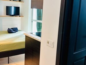 Een kleine kamer met een bed, een televisie op een plank en een raam.