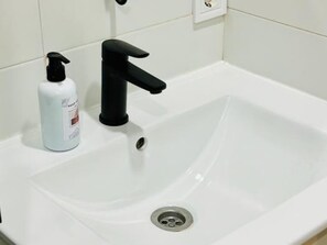 Ein weißes Waschbecken mit einem schwarzen Wasserhahn und einer Seifenspender.