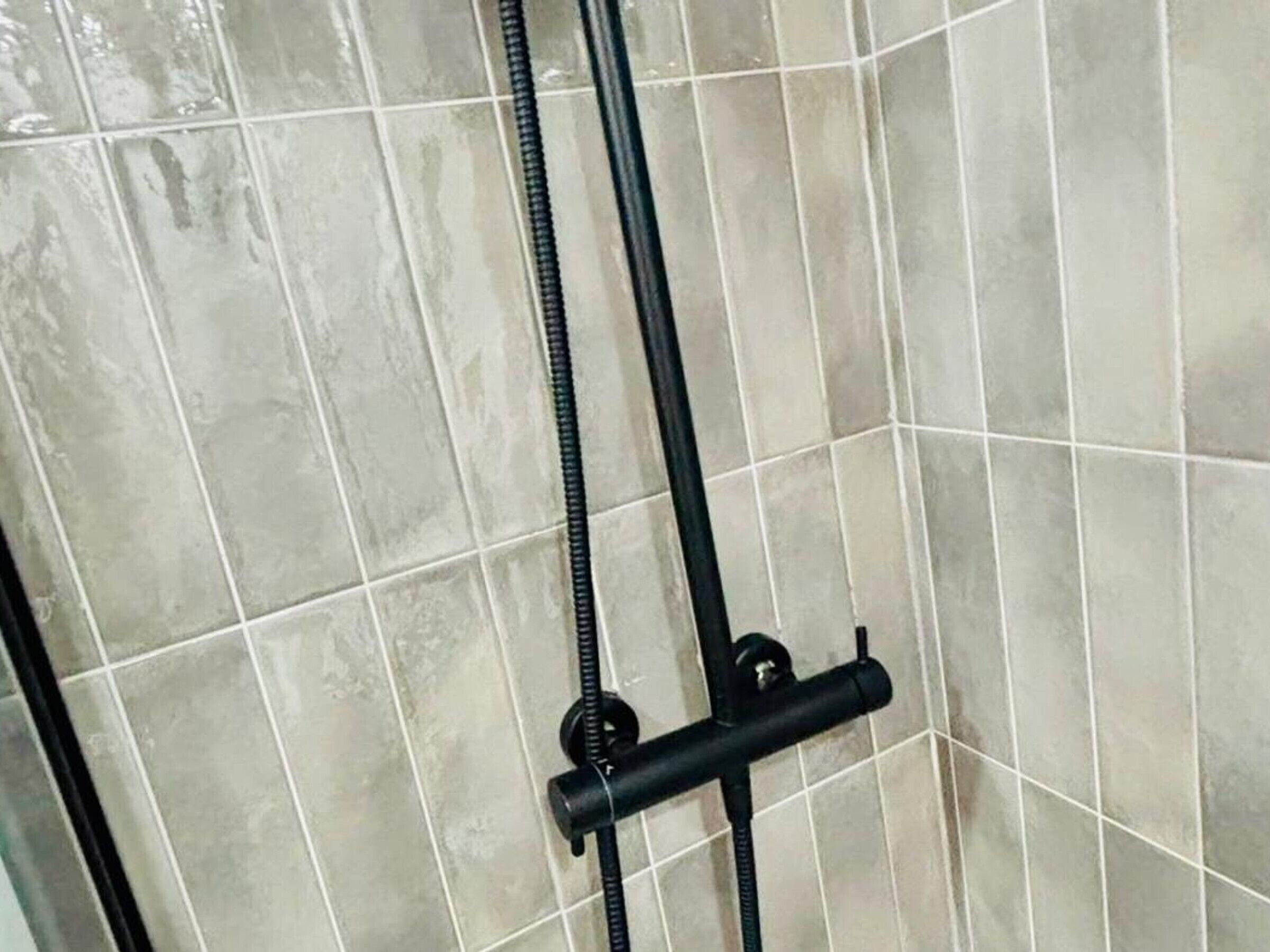 A tiled shower enclosure with a black hose and a control knob.