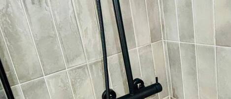 A tiled shower enclosure with a black hose and a control knob.