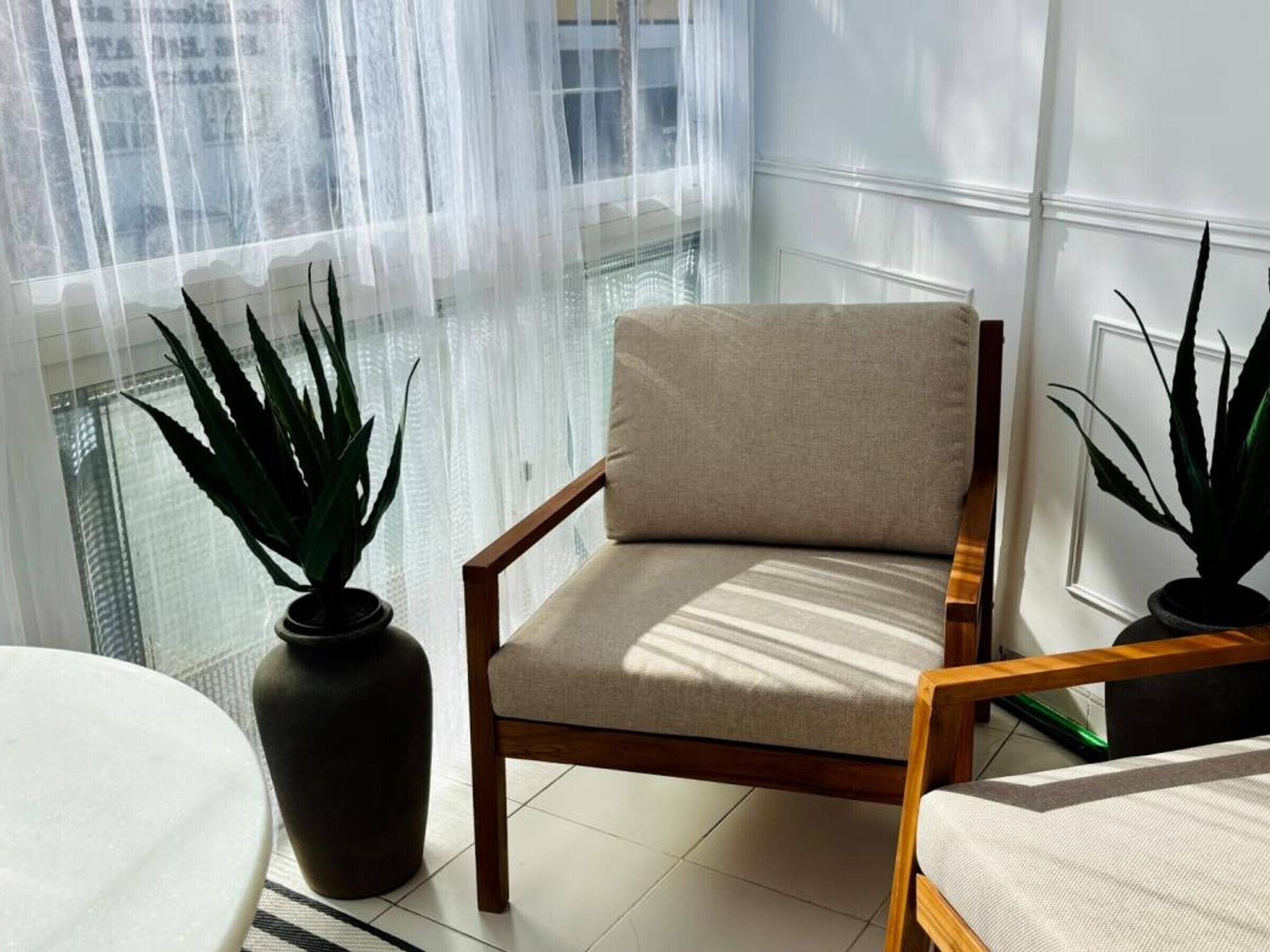 Ein Zimmer mit einem Holzstuhl, einer Topfpflanze und Blick durch ein Fenster mit transparenten Vorhängen.