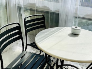 A round table with a white surface and a small white object on it, surrounded by two black chairs with horizontal slats.