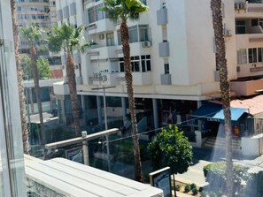 A multi-story building with balconies, palm trees, and a storefront with a blue awning.