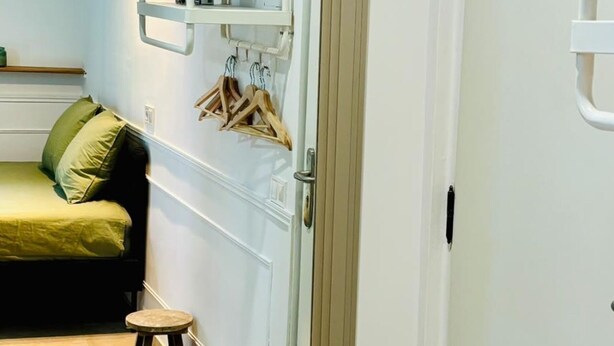 Ein Zimmer mit einem Bett, einem Hocker und einer Tür.