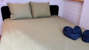 Ein Bett mit einer beigen Bettdecke, zwei Kissen, einem hölzernen Kopfteil und einem Paar blau gefalteter Handtücher.