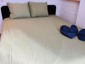Ein Bett mit einer beigen Bettdecke, zwei Kissen, einem hölzernen Kopfteil und einem Paar blau gefalteter Handtücher.