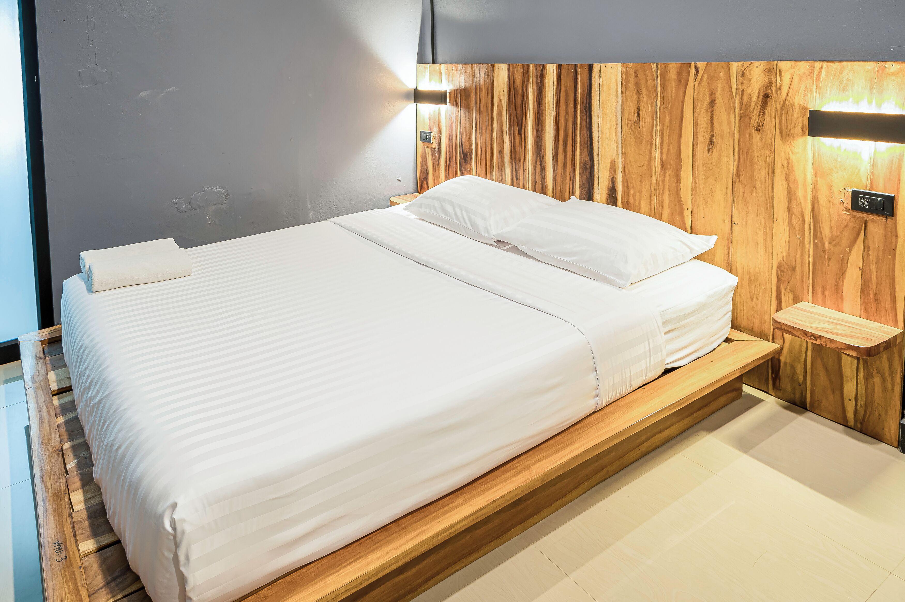 A modern bedroom with a wooden headboard, a large bed with white linens, and a bedside table with a lamp.