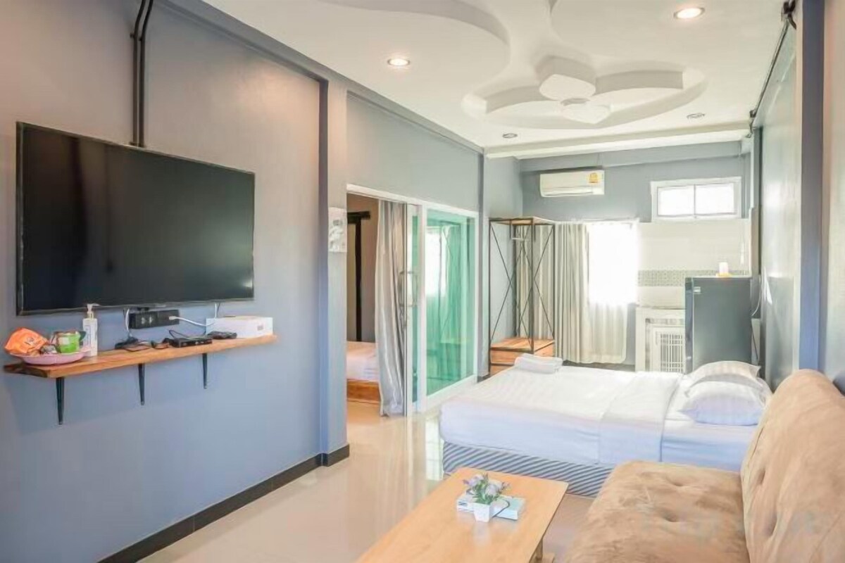A modern hotel room with a flat-screen TV, a sofa, a bed, and a kitchenette.