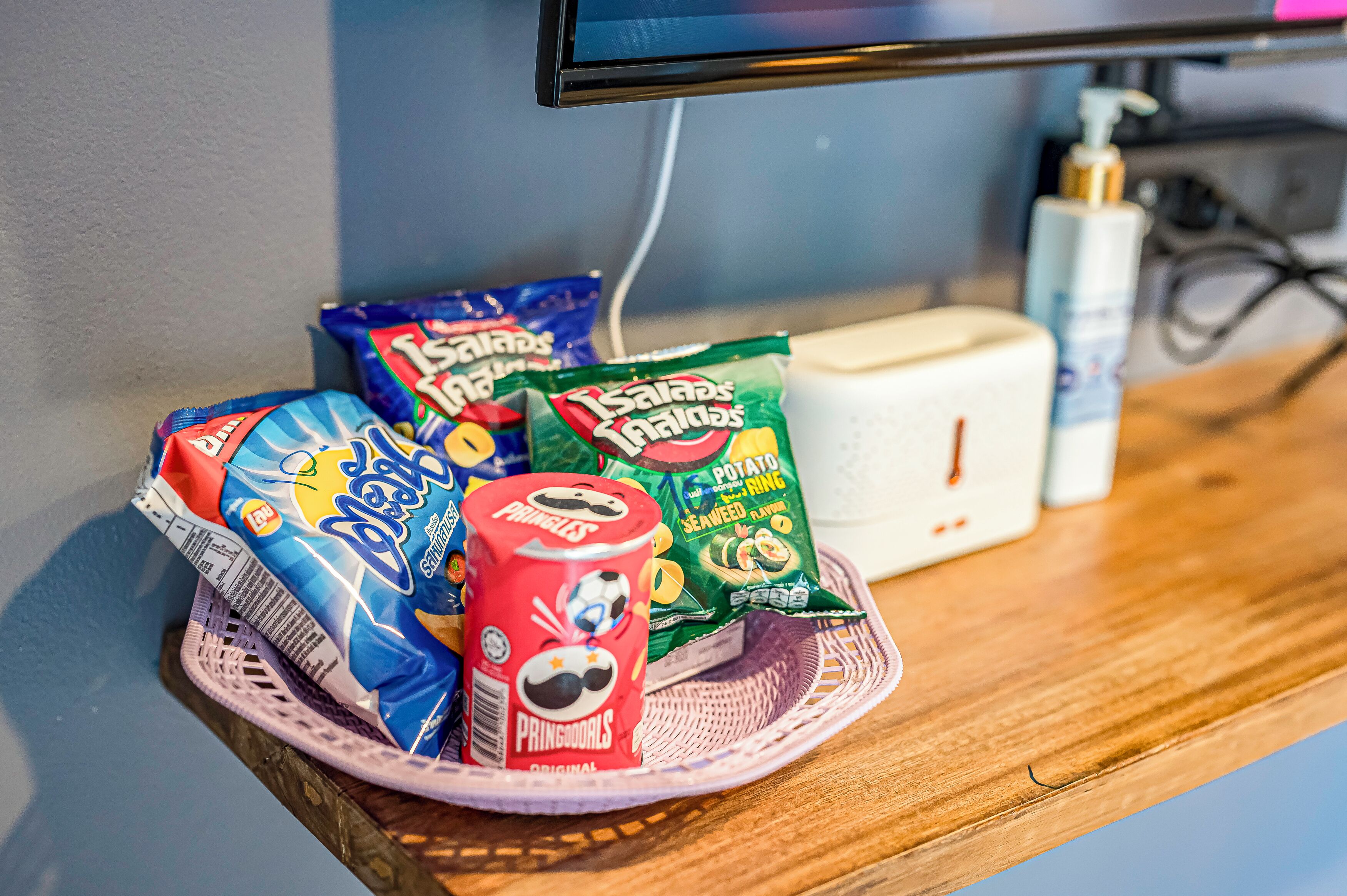A snack basket with chips and a can of Pringles on a wooden table.