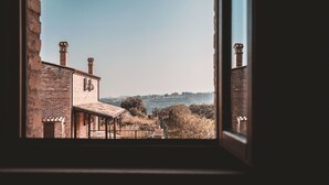 A view through a window of a brick building with a covered porch and chimneys. - Torre di Palme apartment with panoramic terrace and pool -5 minutes from the sea (Marche)