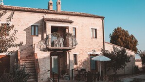 A two-story brick building with a balcony, outdoor seating, and a gravel driveway. - Torre di Palme apartment with panoramic terrace and pool -5 minutes from the sea (Marche)