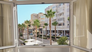 Une vue depuis une fenêtre d’un immeuble, avec des palmiers, une rue et d’autres bâtiments.