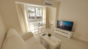 Un salon moderne avec un canapé, une table basse, un téléviseur et un balcon équipé d’une table et de chaises.