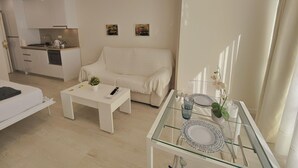 Un salon moderne avec un canapé blanc, une table basse en verre et un coin repas avec une table en verre, mise pour deux personnes.