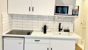 Ett kompakt kök med vita skåp, en svart spis, en mikrovågsugn och ett handfat.