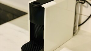 En vit elektronisk apparat med en svart frontpanel, troligen en kaffemaskin, placerad på en vit bänkskiva.