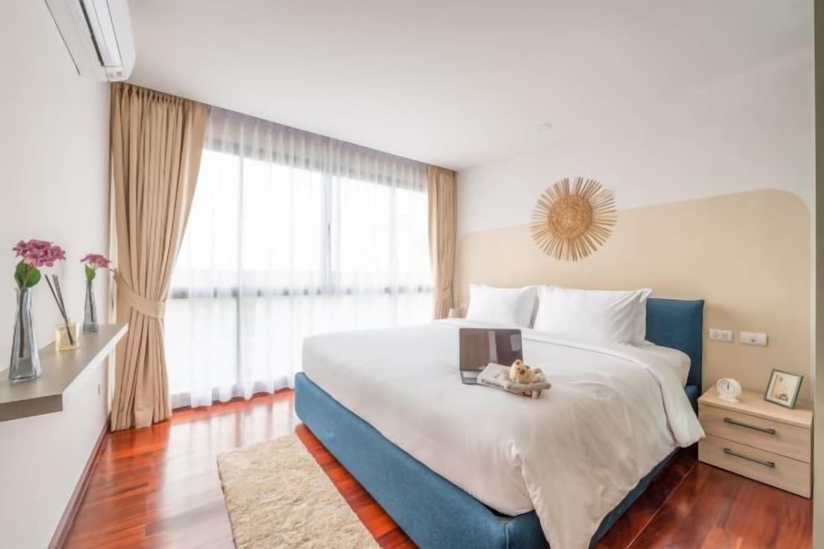 Una habitación de hotel con una cama grande, mesitas de noche y un ventanal con cortinas.