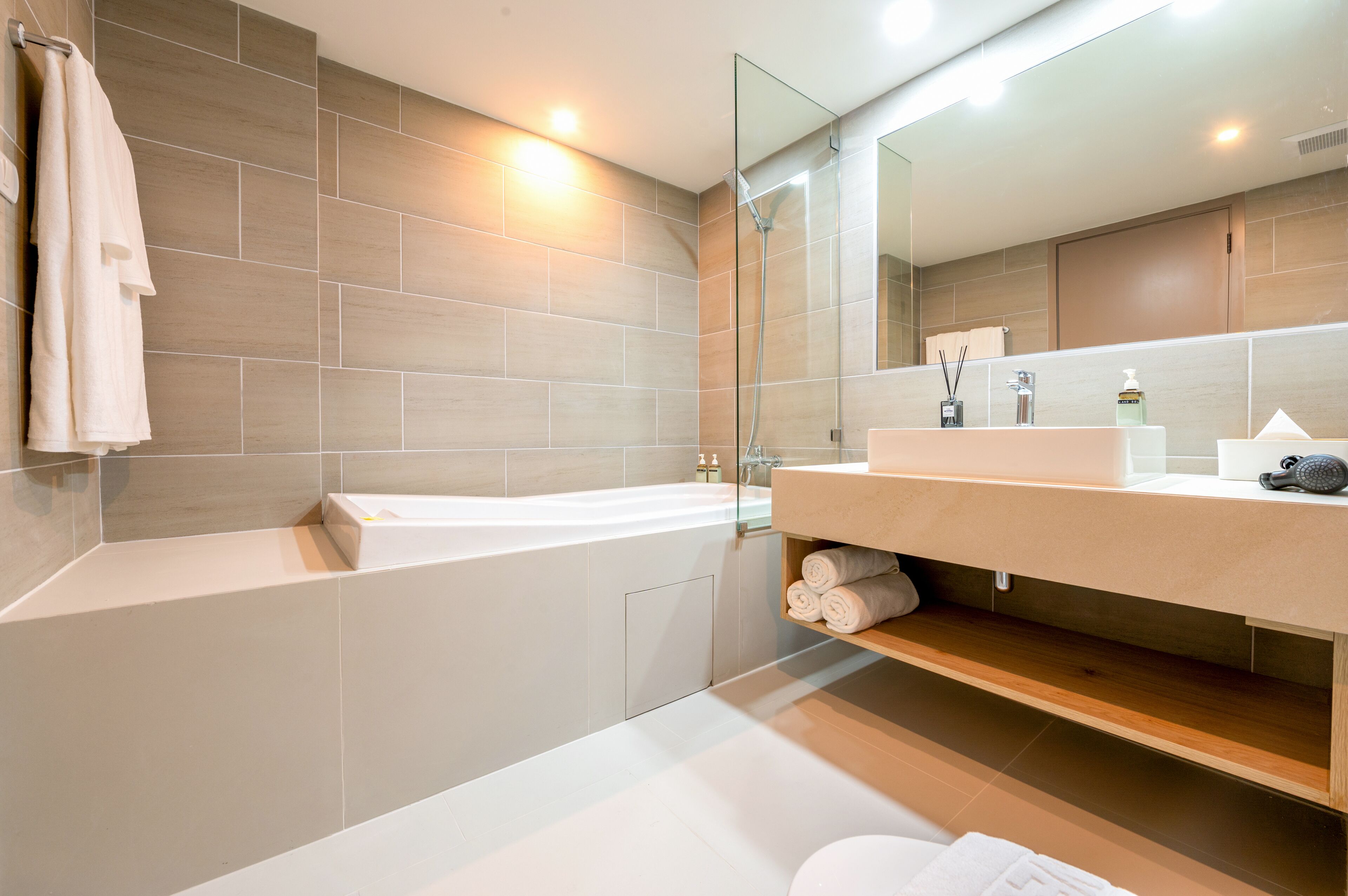 Une salle de bain moderne avec une baignoire, un grand miroir et un meuble-lavabo doté d’un évier et d’un espace de rangement pour les serviettes.
