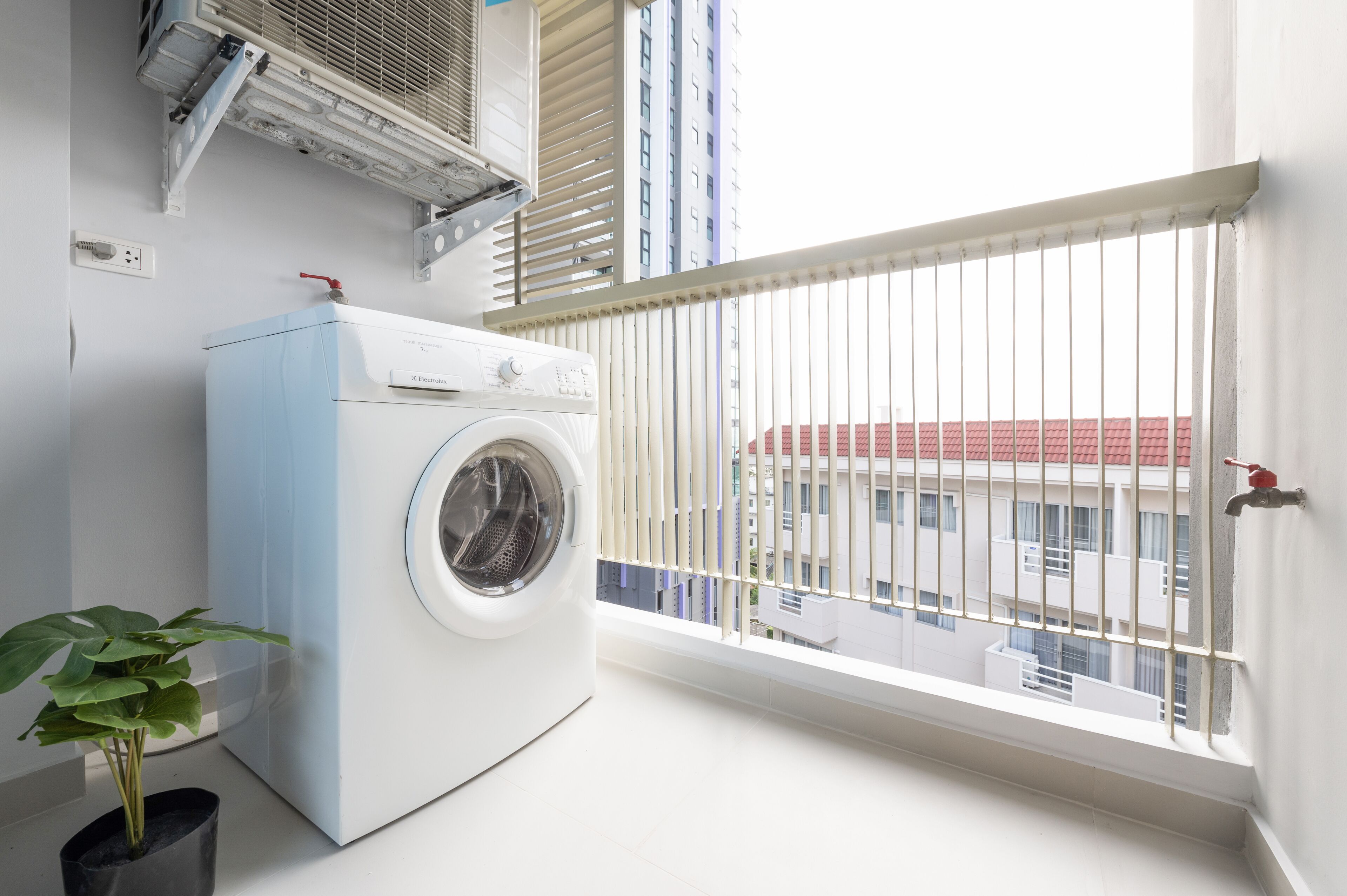 A laundry room with a washing machine, a potted plant, and a window with a view of buildings.