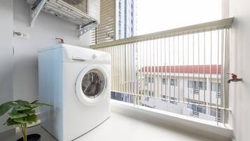 A laundry room with a washing machine, a potted plant, and a window with a view of buildings.