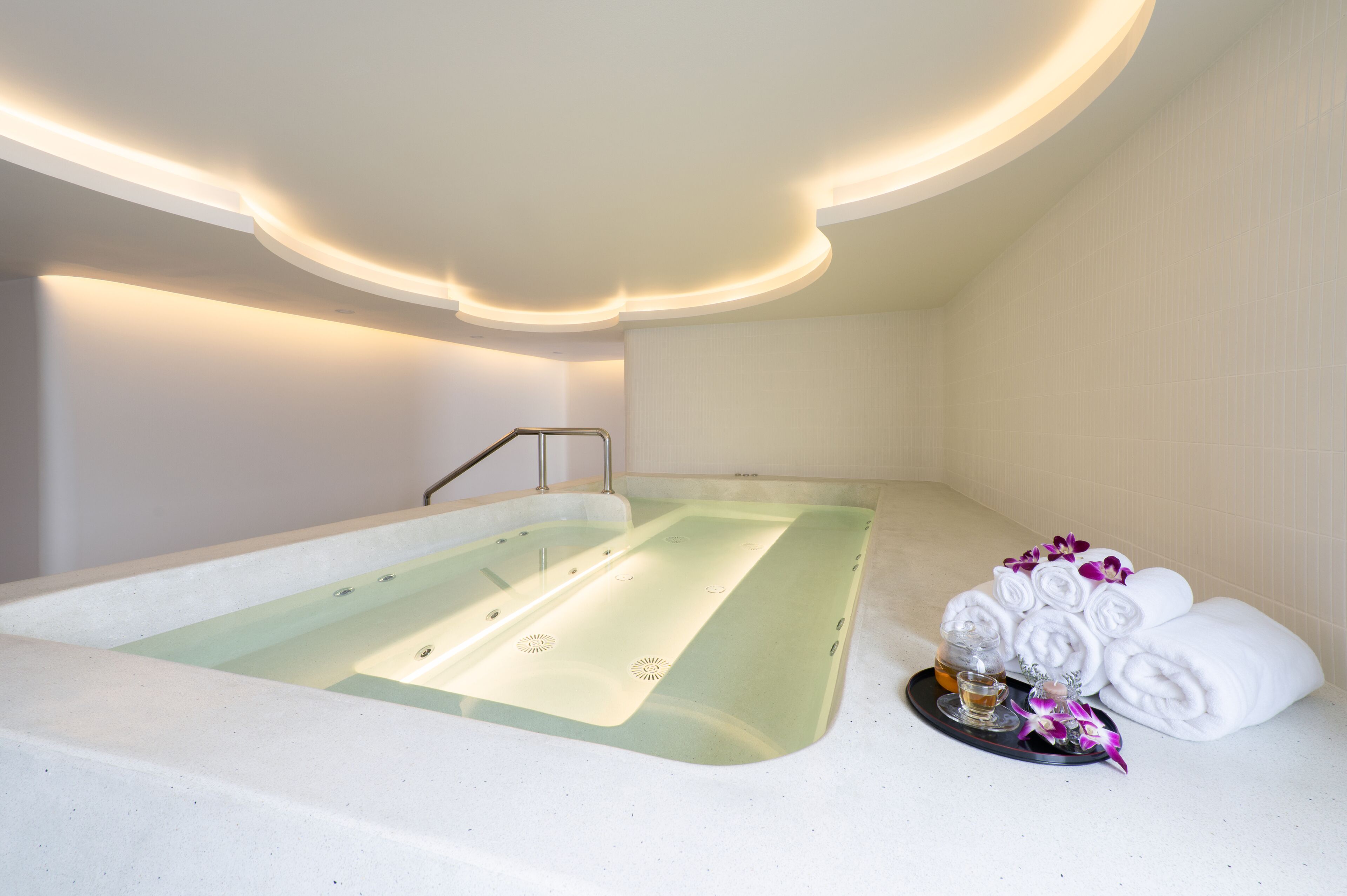 Un cuarto de spa con una bañera, una bandeja con toallas y una bebida, y un perchero para toallas en la pared.