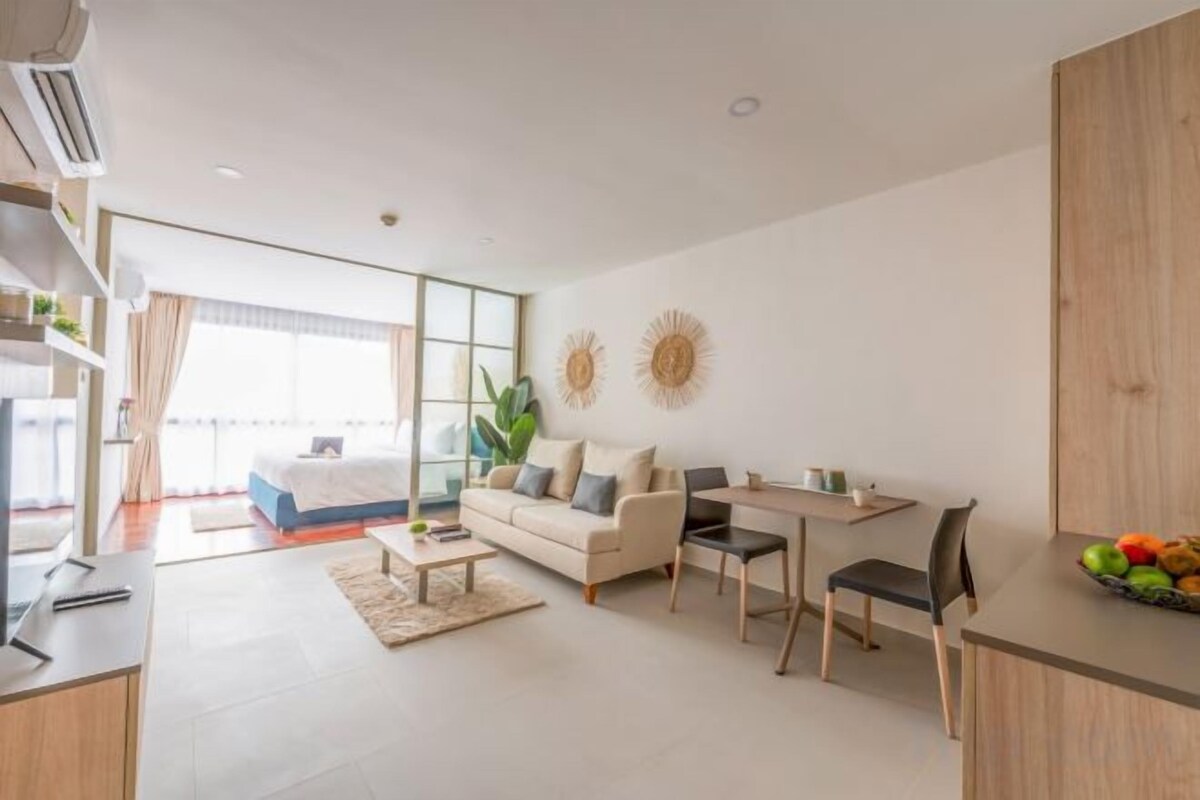A modern hotel room with a bed, a sofa, a dining area, and a kitchen counter.
