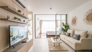 A modern living room with a flat-screen TV, a sofa, a coffee table, and a large window. - HOMA Si Racha (Si Racha)