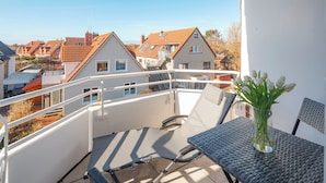 A balcony with a table and chairs, a glass vase with flowers, and a view of neighboring houses. - // Dünensand Norderney // (Norderney)