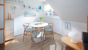 A cozy dining area with a round table, four wooden chairs, and a vase with flowers. - // Dünensand Norderney // (Norderney)