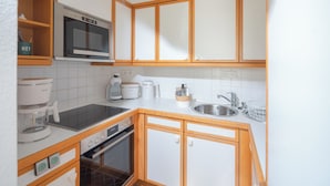 A compact kitchen with white cabinets, a microwave, a coffee maker, and a sink. - // Dünensand Norderney // (Norderney)
