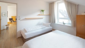 A bedroom with a bed, a window with curtains, a wooden cabinet, and a small plant on a shelf. - // Dünensand Norderney // (Norderney)