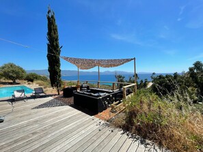 Um deck de madeira com piscina, espreguiçadeiras e vista para o mar e montanhas.