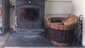 A room with a wood-burning stove, a framed landscape painting, and a wicker basket with bread.