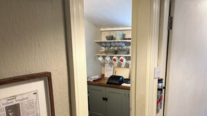 A hallway with a framed obituary, a bottle of wine, and a kitchen area with cabinets and dishware.