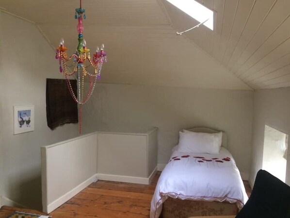 Une chambre avec un plancher en bois, un lit blanc agrémenté de touches de rouge, un lustre et une fenêtre.