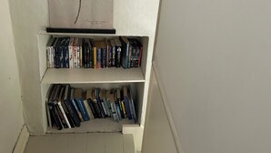 A narrow hallway with a bookshelf filled with books, a framed picture of a plant on the wall, and a wooden floor.
