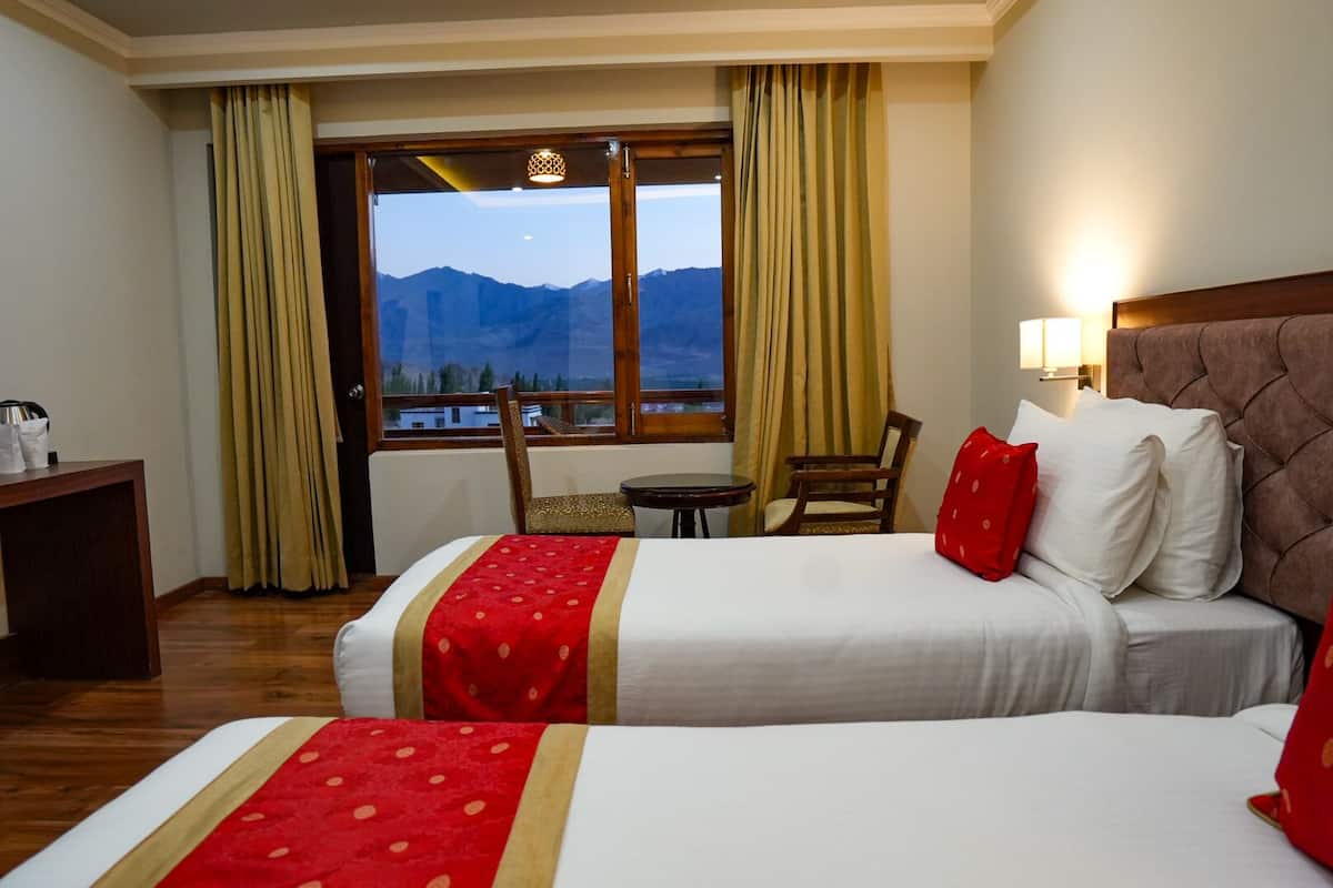 A hotel room with two beds, a desk, a chair, and a view of mountains through the window.