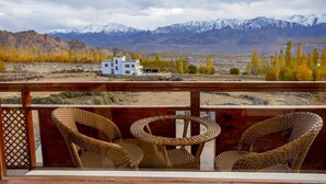 A balcony with wicker chairs and a view of a mountain range. - Hotel Karma Residency (Leh)