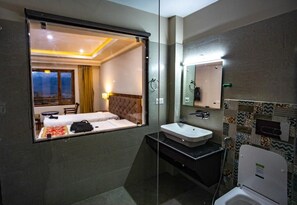 A hotel room with a bed, a bathroom with a sink and toilet, and a large mirror. - Hotel Karma Residency (Leh)